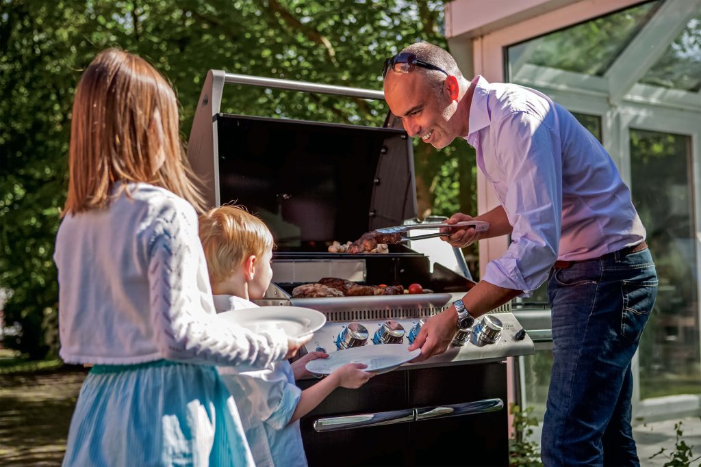 Foto: man met twee kinderen bij een grill van Napoleon. De foto hoort bij de 10 tips voor bbq-seizoen 2018.
